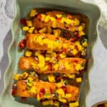 A green ruffled baking dish with four fillets of pan seared salmon topped with sweet chili sauce and mango salsa.