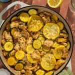 A skillet filled with lemon chicken, zucchini and summer squash, garnished with parmesan cheese.