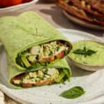 A green goddess rotisserie chicken wrap cut in half and stacked on top of each other with dressing dripping on the front.