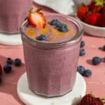 A glass with peanut butter and jelly smoothie swirled with peanut butter and topped with a fresh strawberry and blueberries.