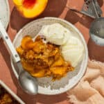 A plate with peach crumble and two scoops of vanilla ice cream.