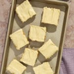 A baking sheet with eight squares of banana bars with brown butter frosting.