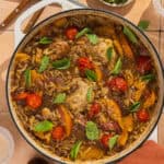 A large skillet of chicken with peaches and orzo garnished with fresh basil.