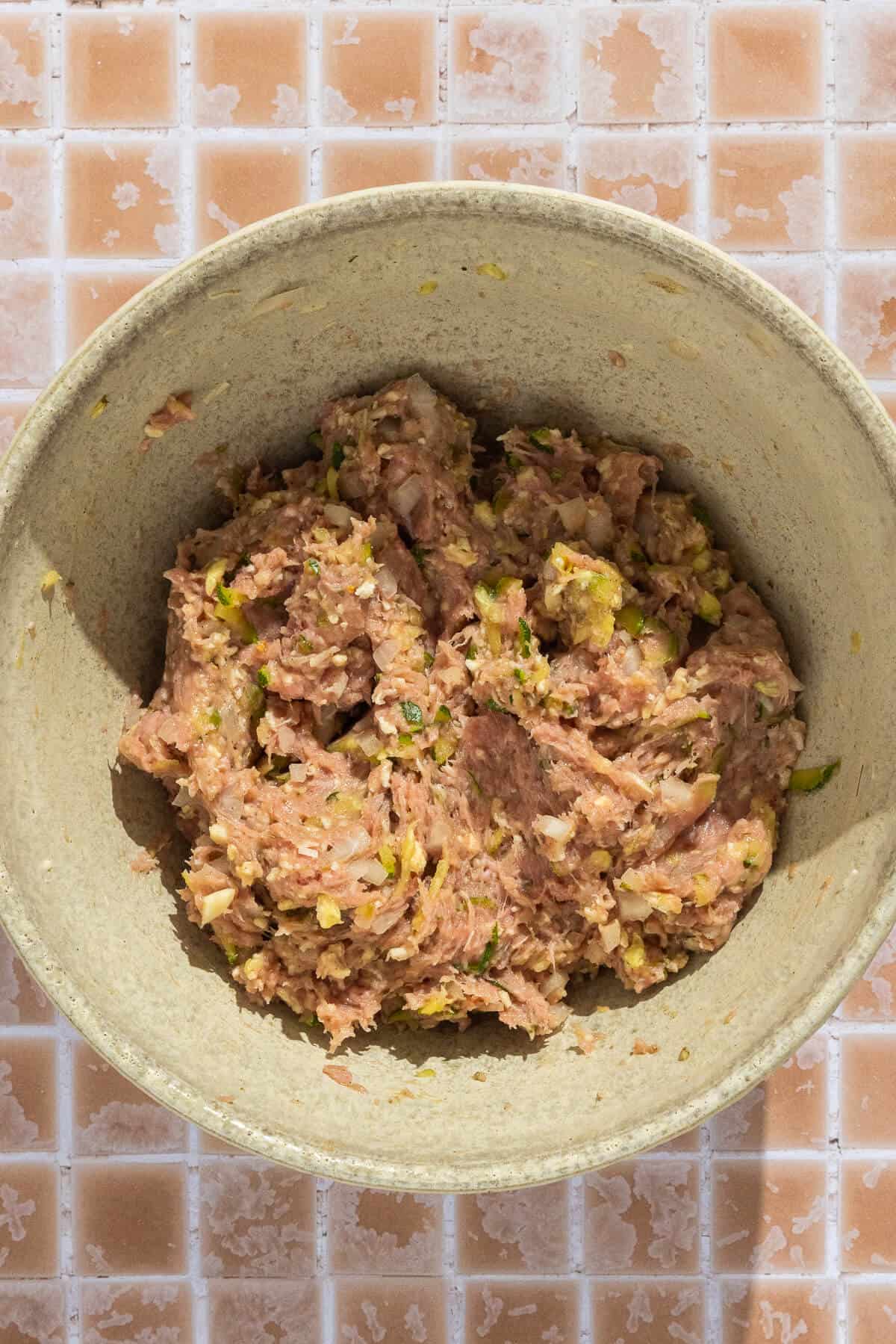 A mixing bowl with ingredients for zucchini turkey meatballs after mixing.