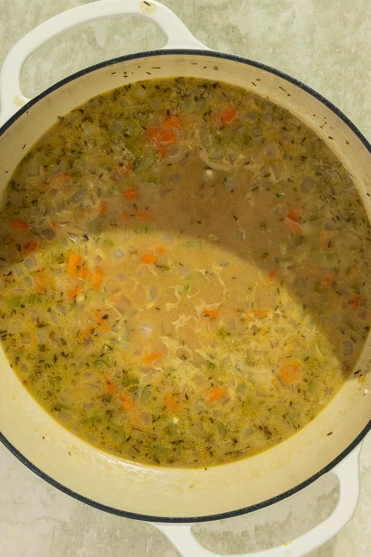 Broth added to the veggies, flour, and spices mixture with the raw chicken breasts nestled into the soup.