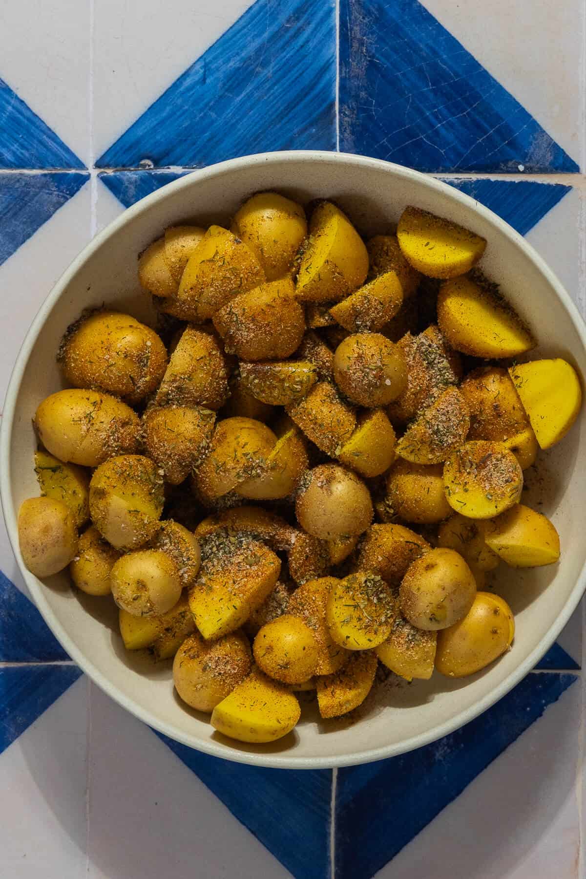 A mixing bowl with cut potatoes with seasonings prior to mixing.