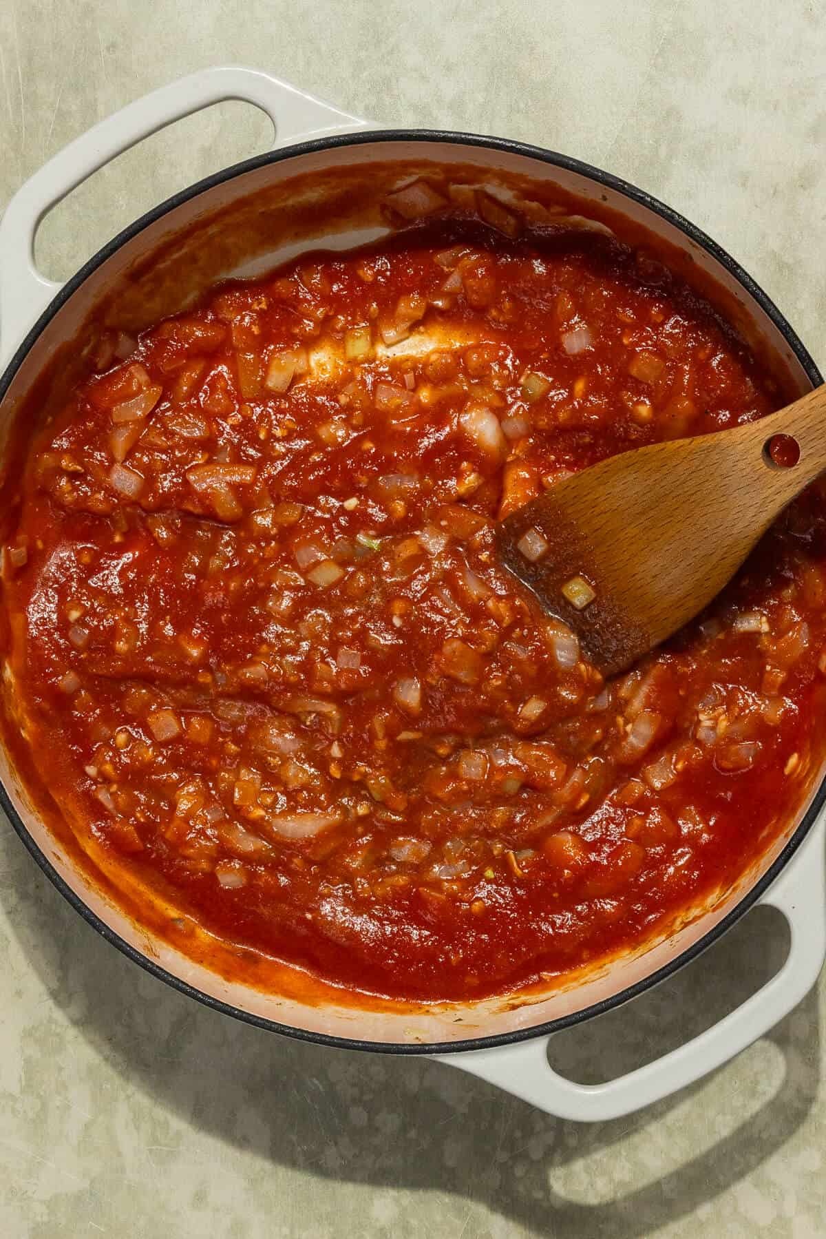 A large skillet with tomato sauce combined with cooked onion and spices.