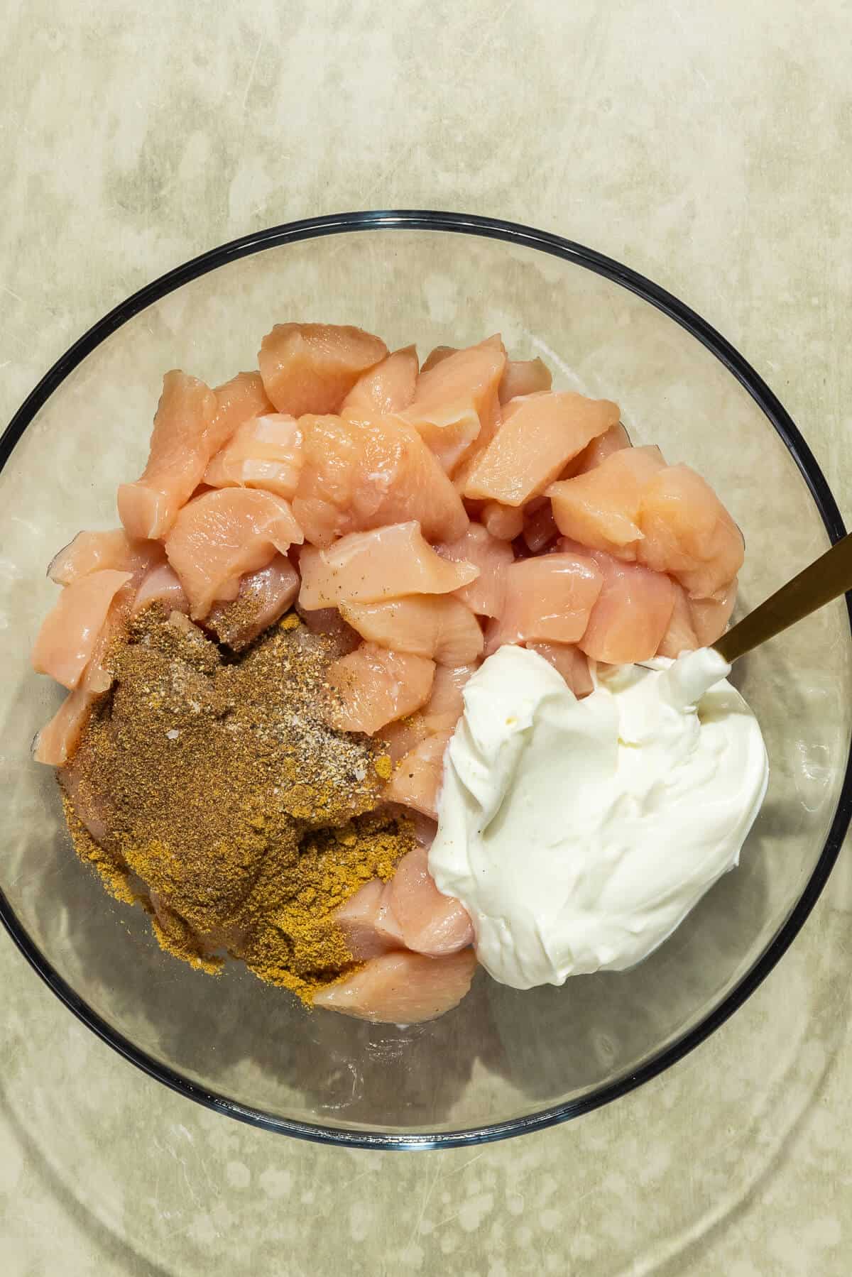 A large mixing bowl with raw diced chicken, yogurt, and spices.