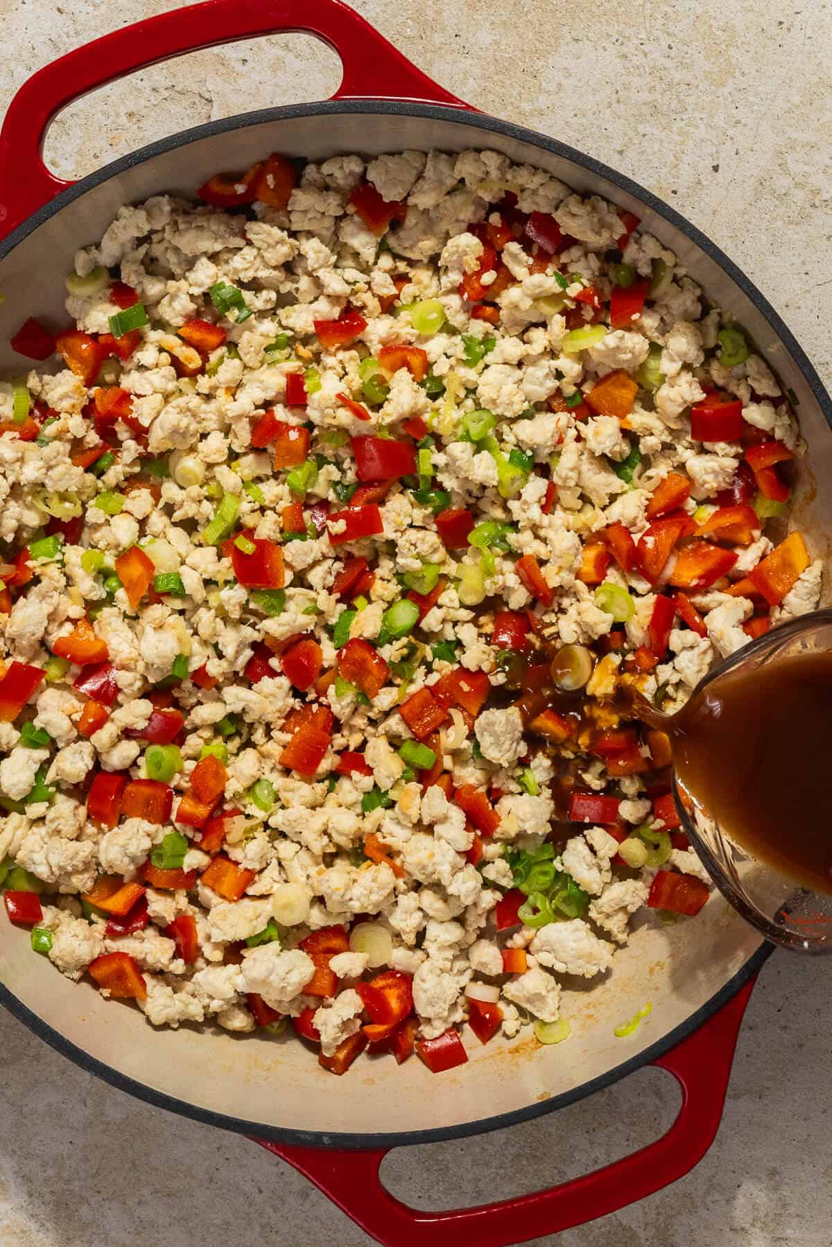 A large skillet with the sauce being added to the cooked ground chicken and veggies.