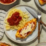 A plate with a piece of chicken parmesan alongside spaghetti noodles and marinara sauce.