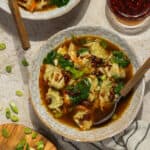 Two bowls of wonton soup topped with chili crisp and sliced green onions.