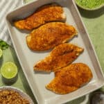 A baking dish with four seasoned and cooked chicken breasts.