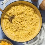 A wooden spoon in a large pot of homemade Mac and cheese.