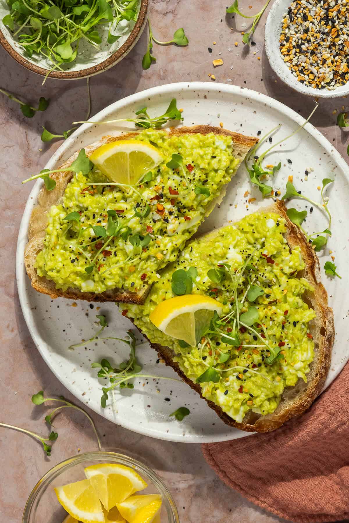 A plate with avocado egg salad on toasted bread garnished with lemon and micro greens.