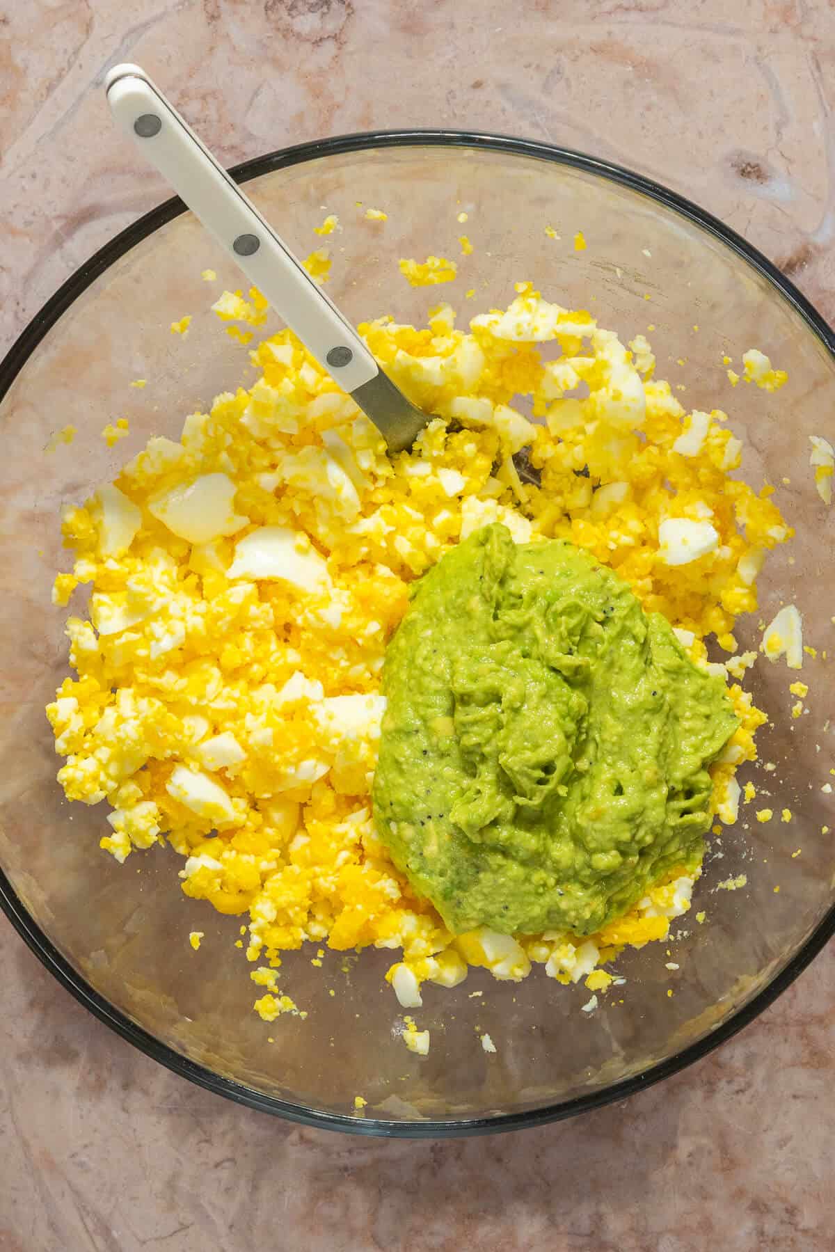 Mashed avocado added to a bowl of mashed hard boiled eggs.