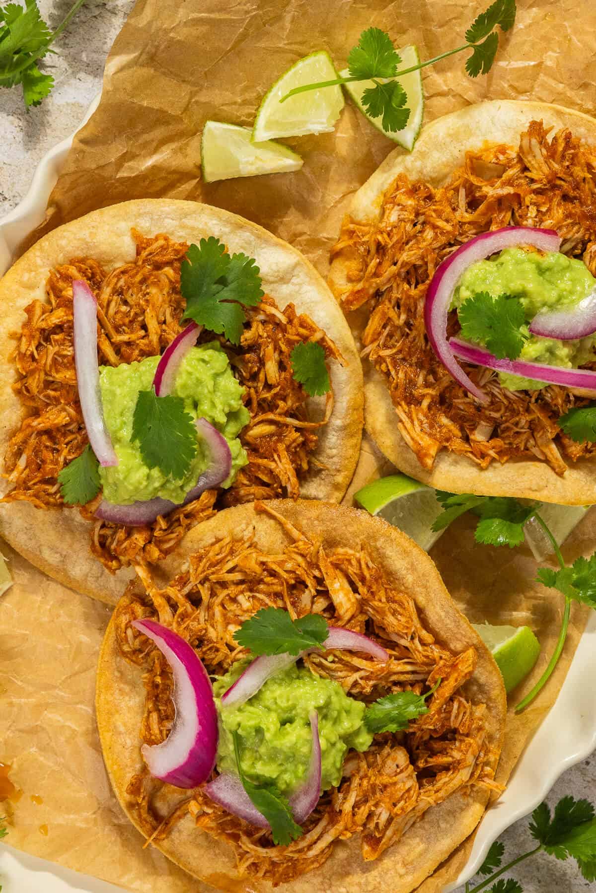 Three chicken tinga tostadas topped with guacamole, pickled onions, and cilantro.