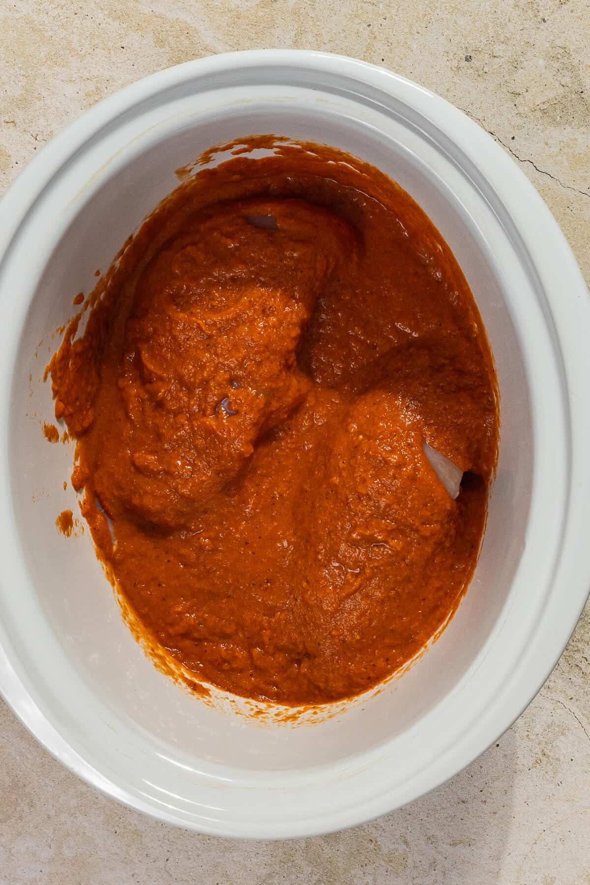 A crockpot insert with the tinga sauce poured over the raw chicken breasts.