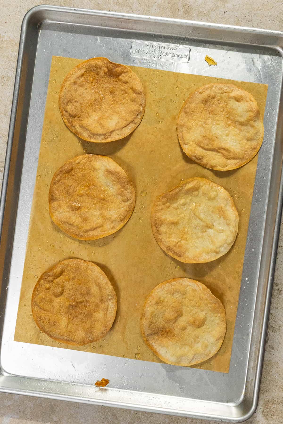 A parchment-lined baking sheet with six baked corn tortillas to use as tostadas.