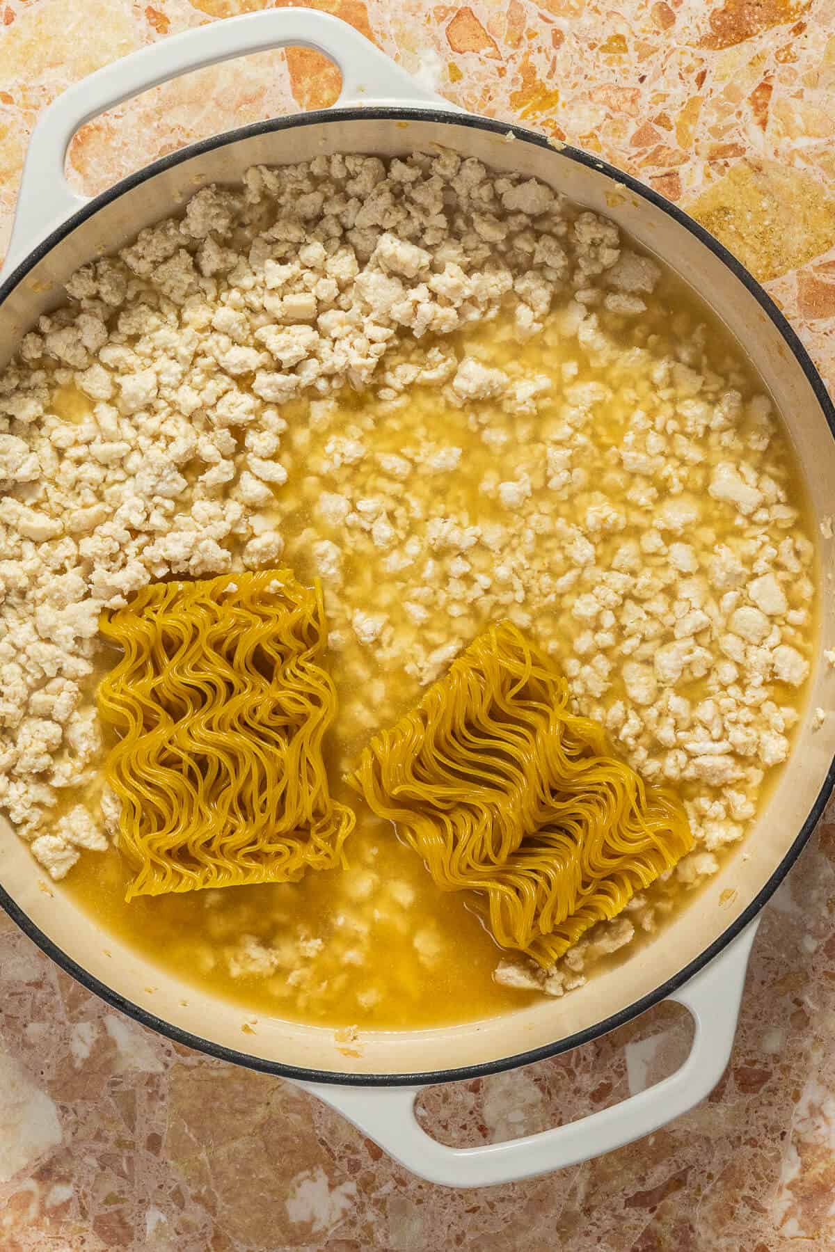 Ramen bricks added to a large pan of ground chicken with chicken broth.
