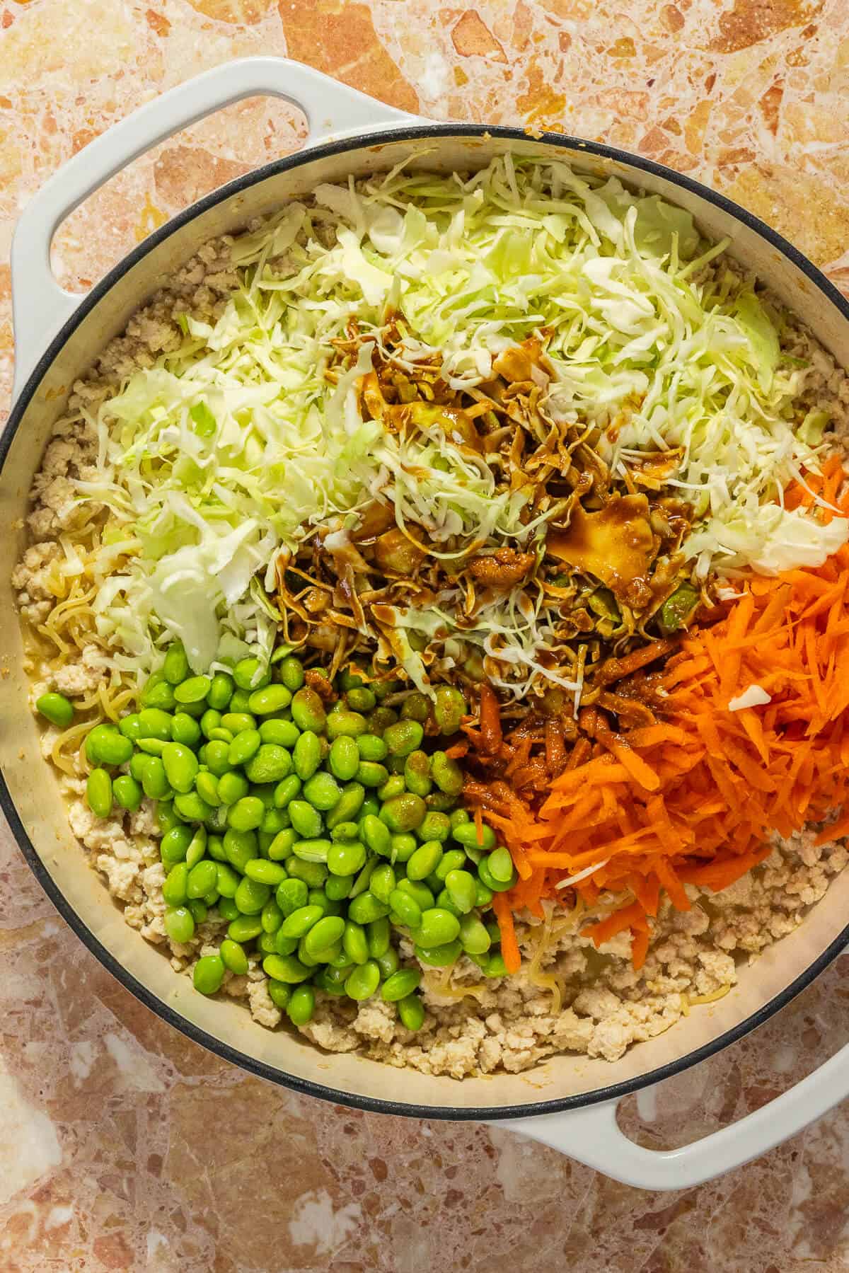 Edamame, cabbage, shredded carrots, and sauce added to the pan of cooked ground chicken and noodles.