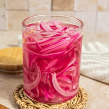 An open jar of pickled red onions on a woven coaster.