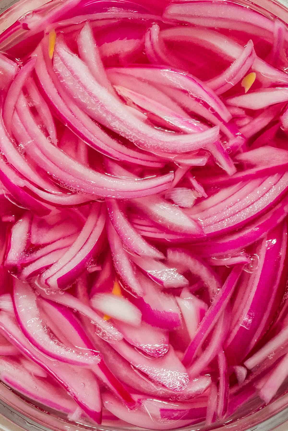 A close up image of pickled red onions.