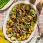 A platter of sheet pan pork tenderloin and potatoes topped with basil and served alongside asparagus.