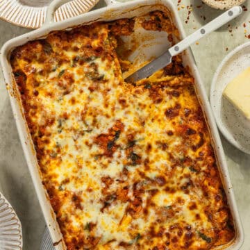 A baking dish of lasagna with a piece cut out of it.