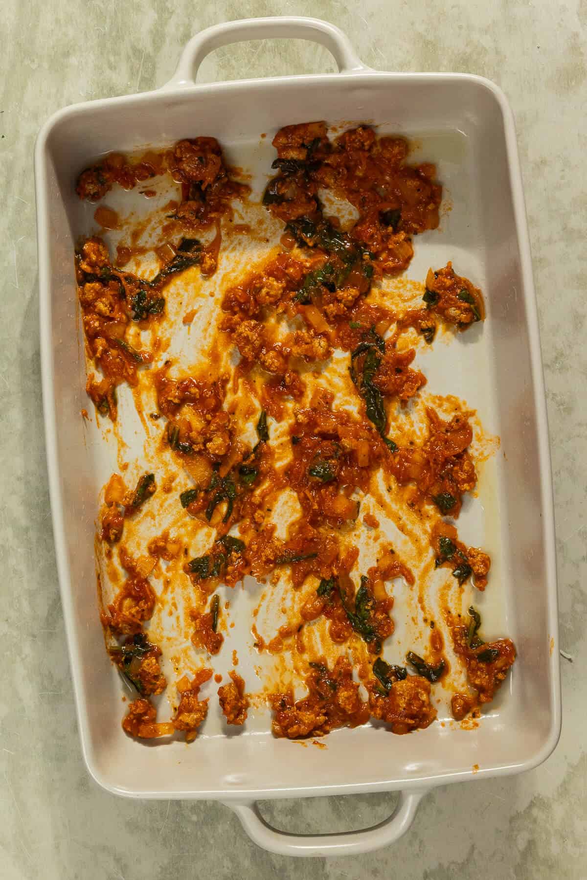 A small amount of the meat mixture added to the bottom of a baking dish for the cottage cheese lasagna recipe.