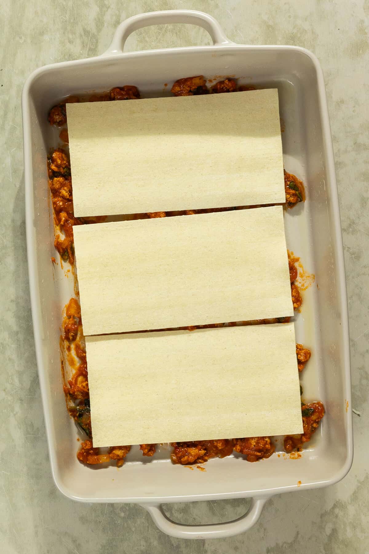 Three lasagna noodles on top of the meat mixture in a baking dish.