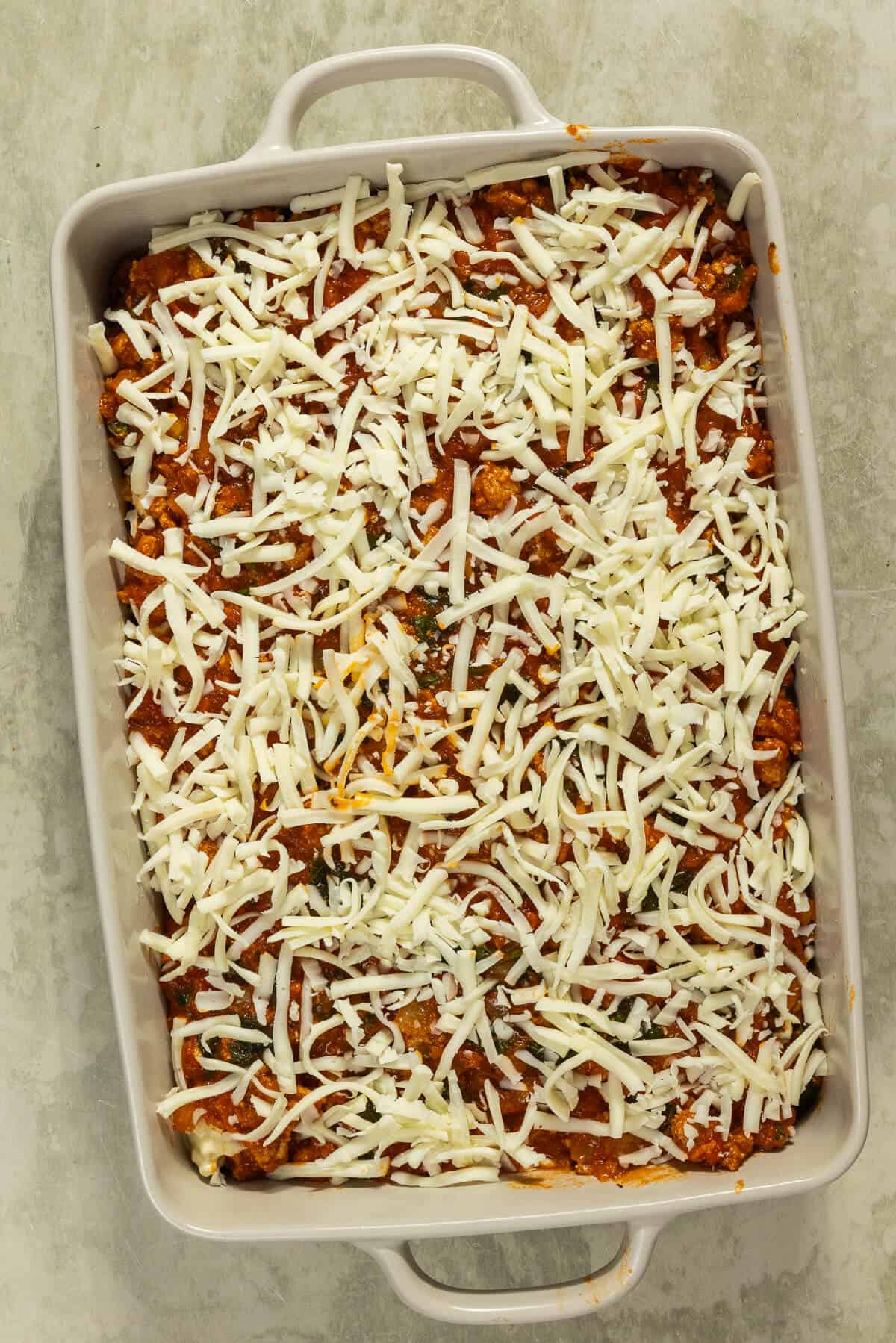 Shredded cheese added to the top of the assembled lasagna.