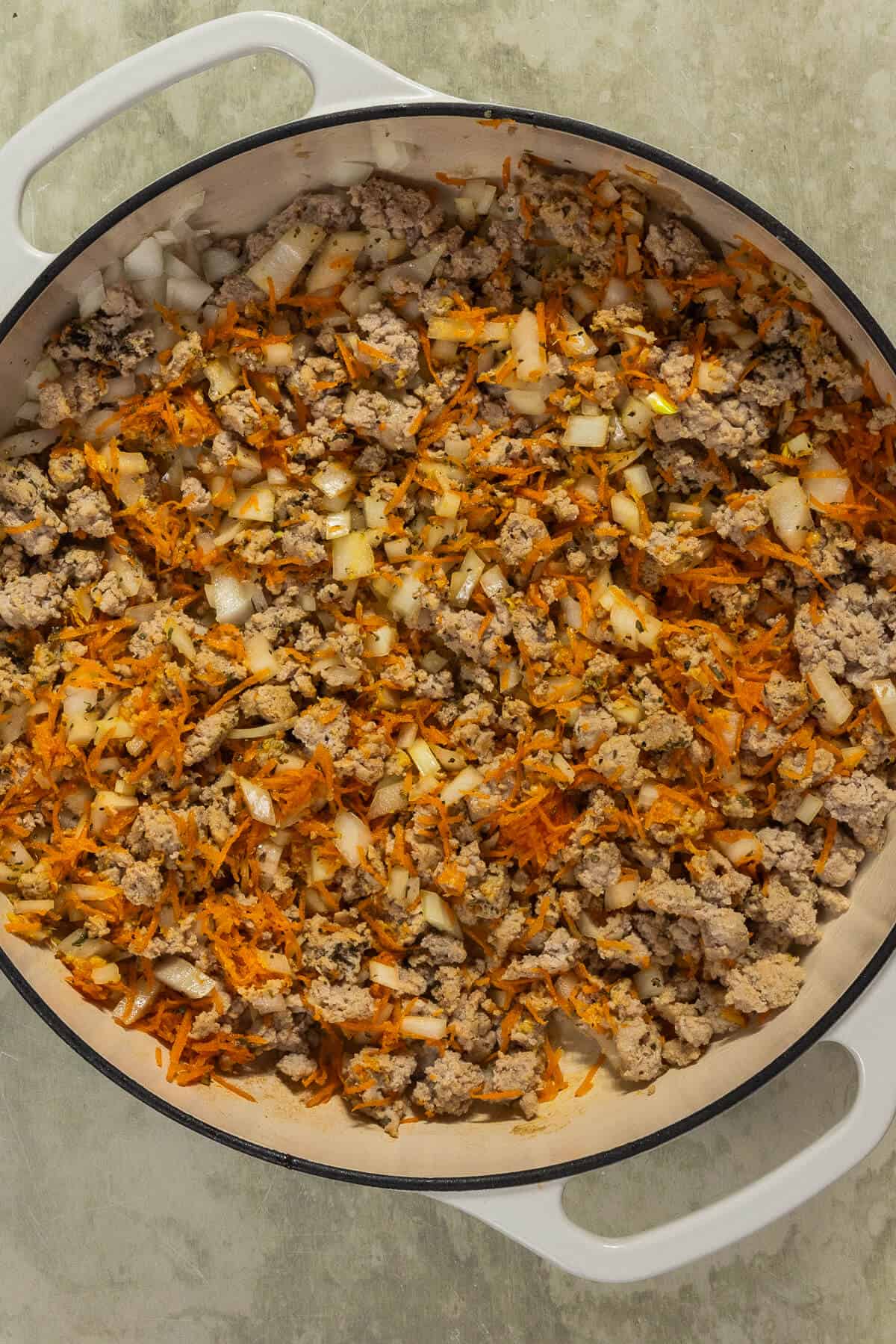 A large skillet with cooked ground turkey, shredded carrots, and onions.