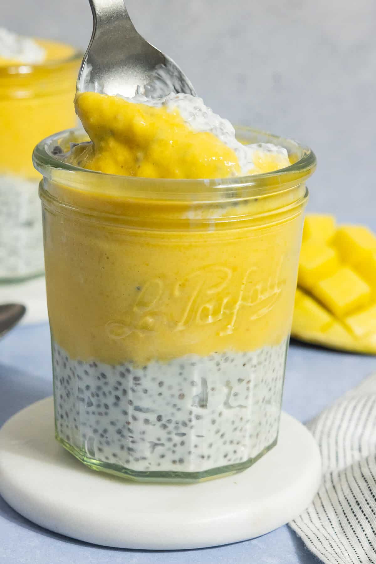 A glass jar of layered mango chia pudding with a spoonful on a spoon.