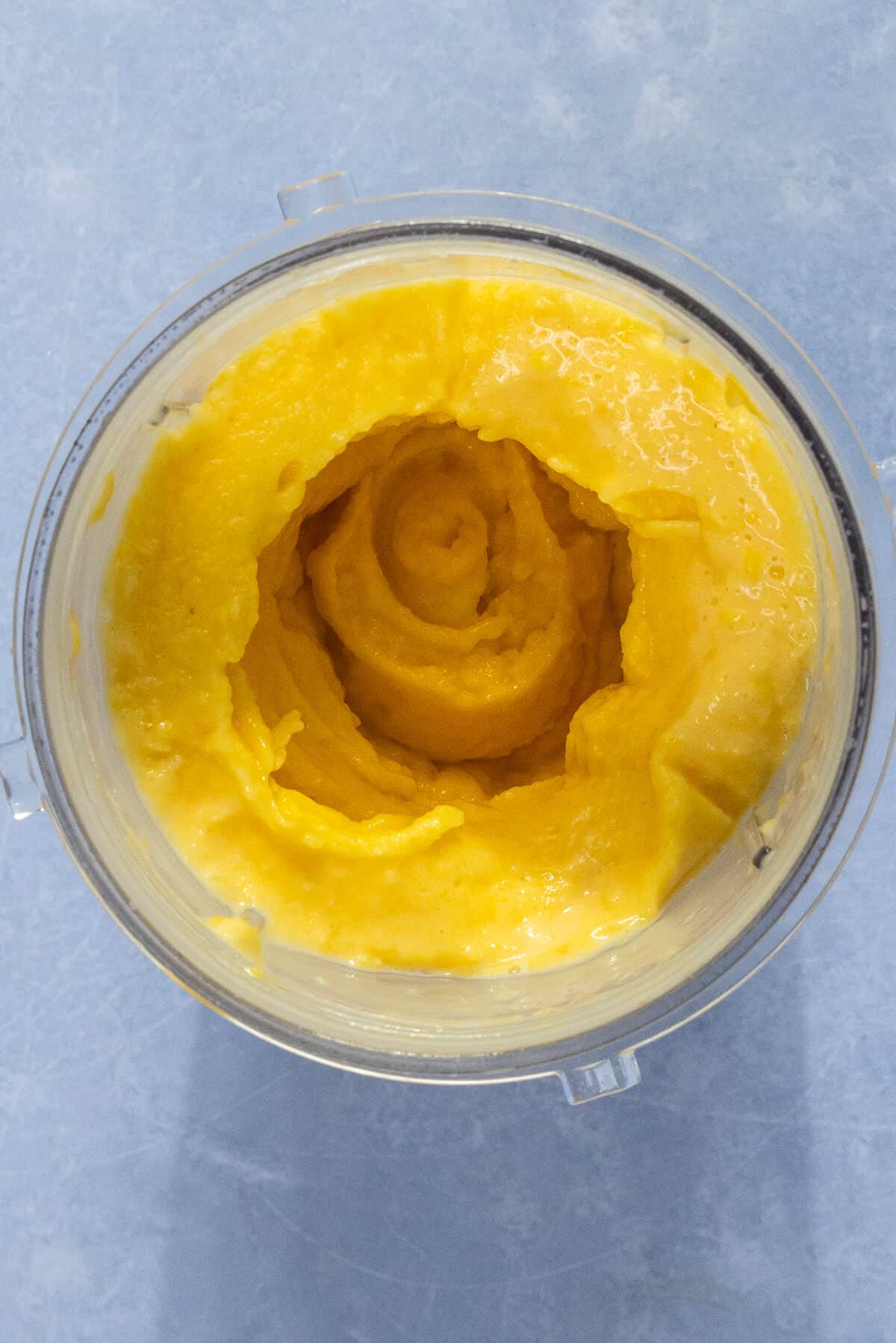 A handheld blender with mango and coconut milk blended together.