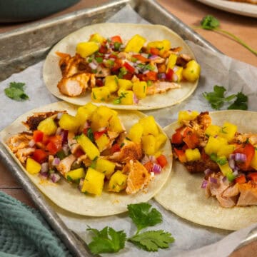 Three assembled salmon tacos with pineapple salsa on a baking sheet.