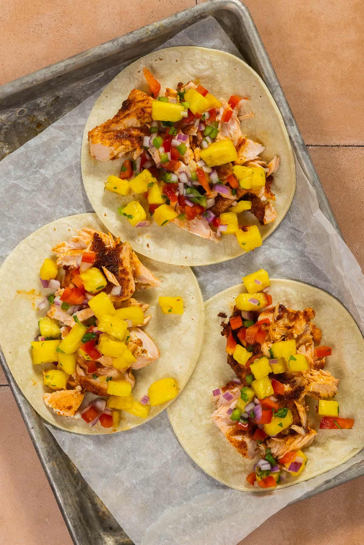A baking sheet with three assembled salmon tacos with pineapple salsa.