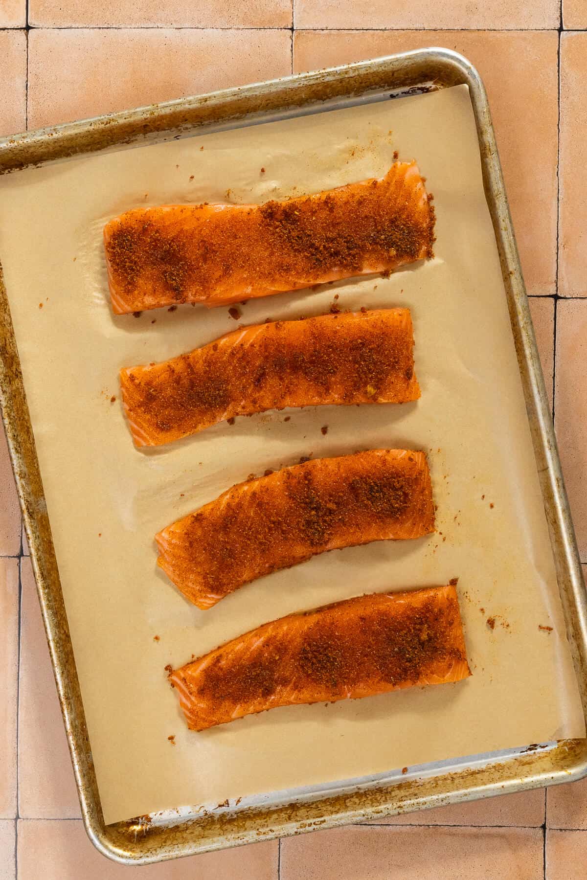 A parchment lined baking sheet with four seasoned salmon filets prior to baking.