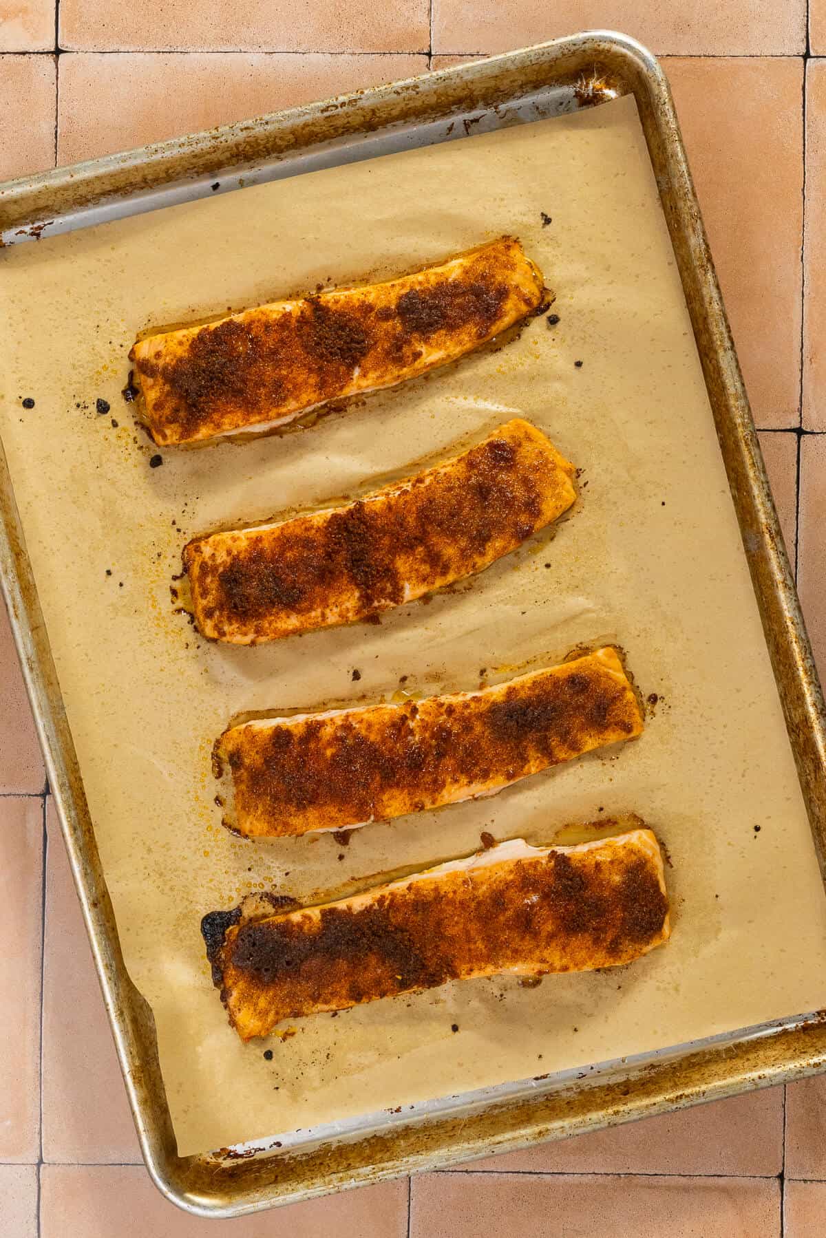 A parchment lined baking sheet with four seasoned salmon filets after baking.