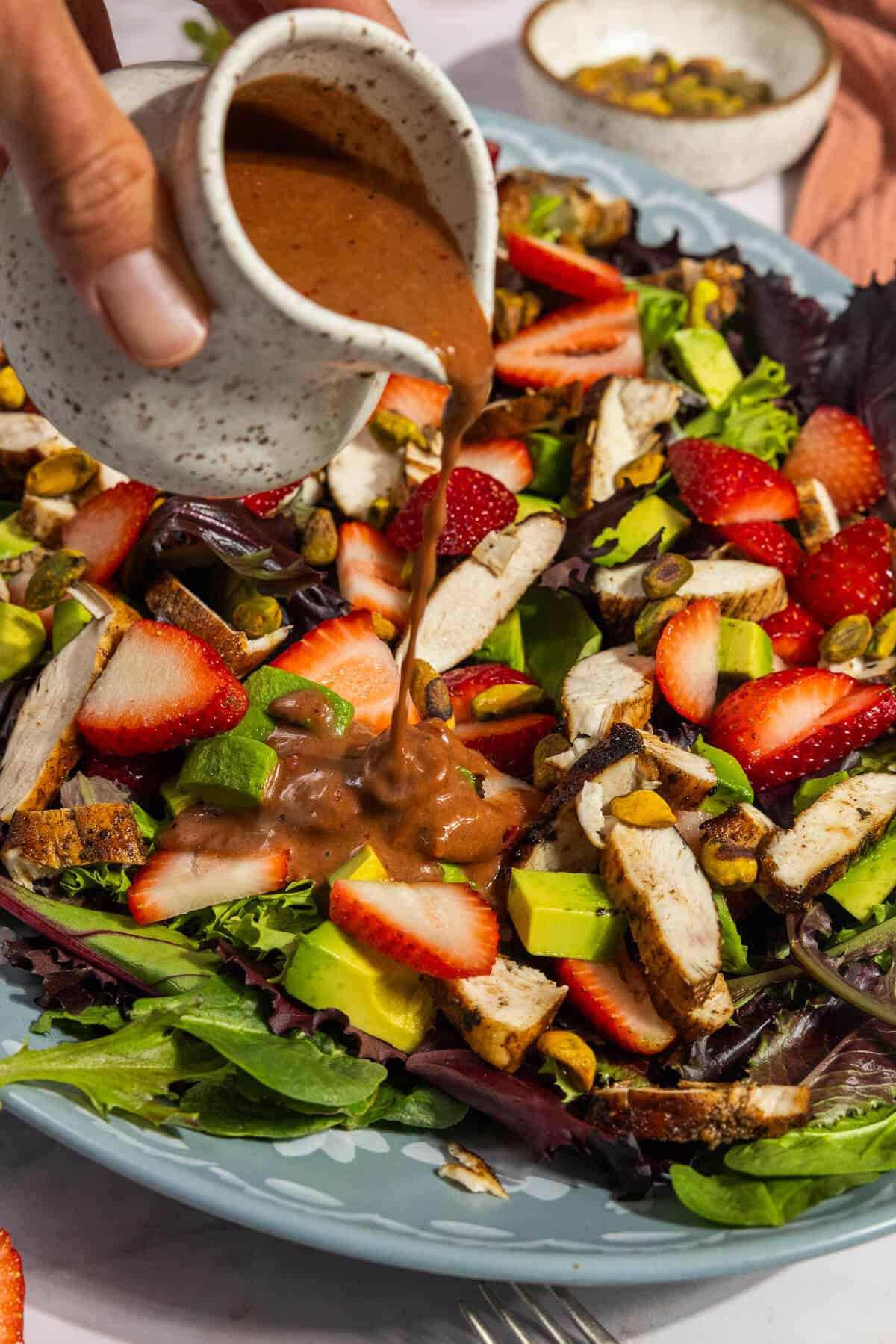 Strawberry balsamic dressing being poured over the strawberry pistachio salad with chicken.