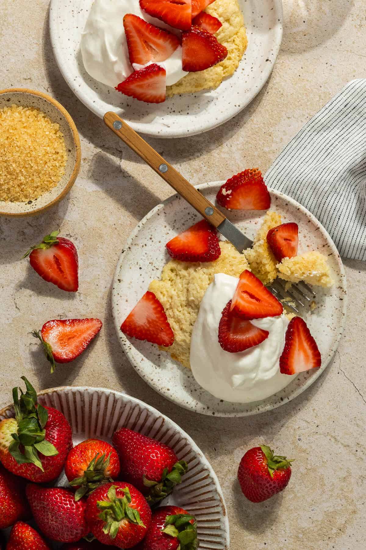 Two plates of strawberry shortcake on biscuits topped with whipped cream and fresh strawberries.