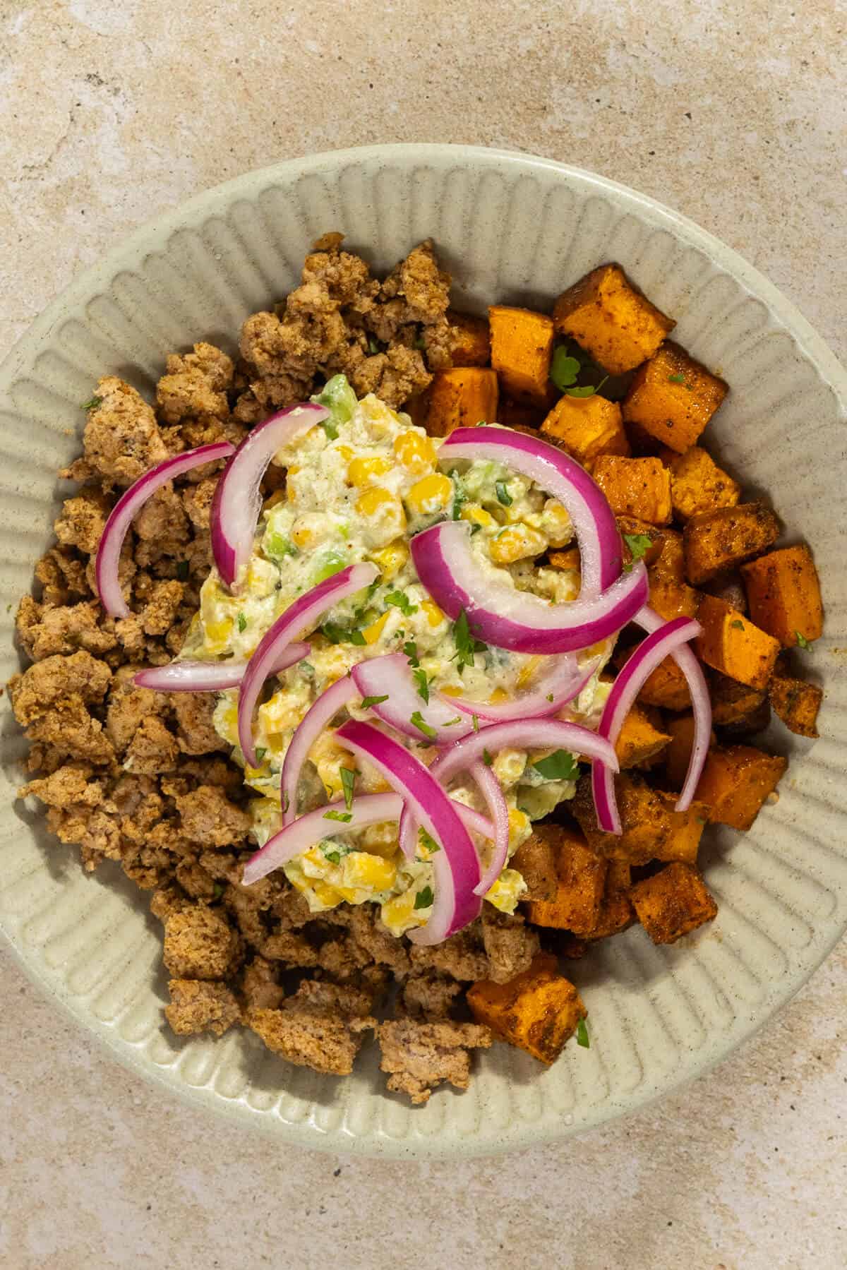 A bowl of roasted sweet potatoes, ground turkey, street corn, and pickled onions.