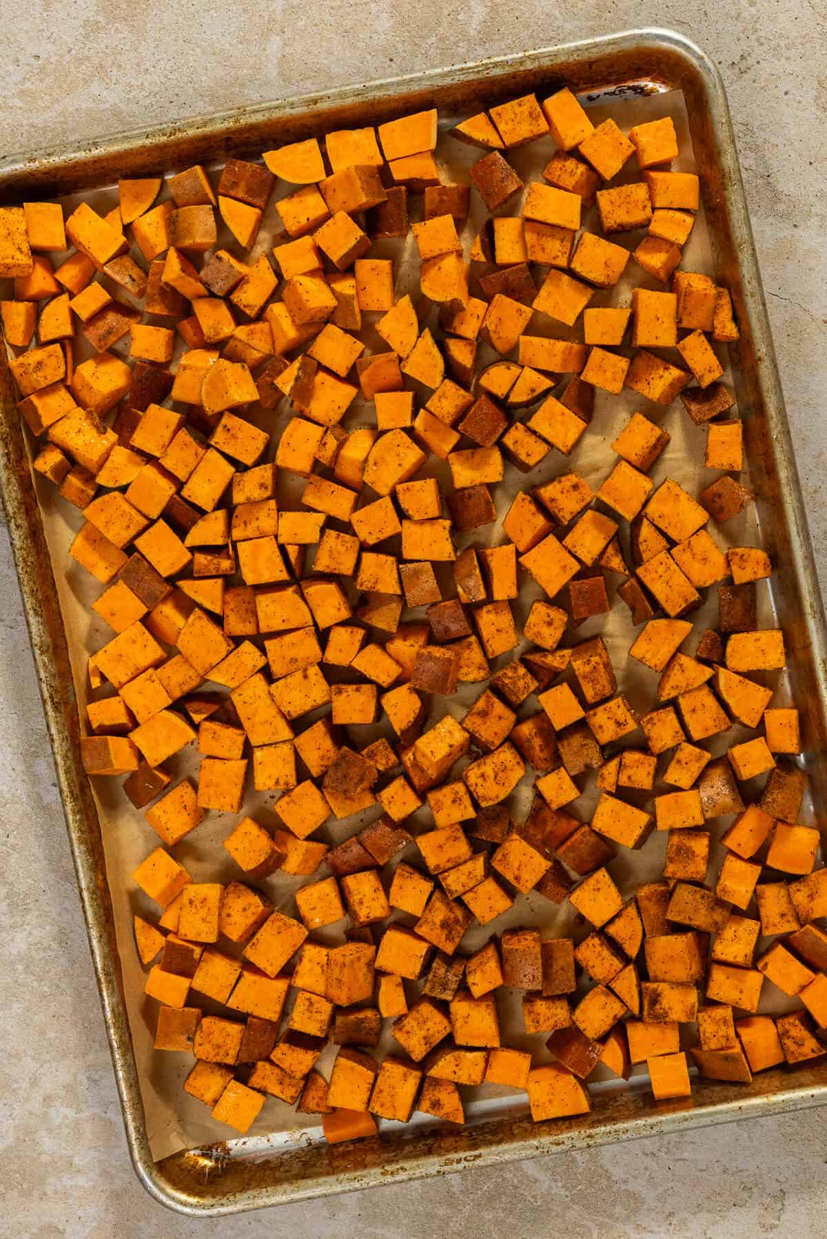 A baking sheet with seasoned sweet potatoes prior to roasting.