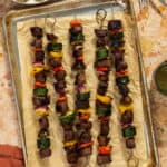 A parchment-lined baking sheet with five beef kabobs lined across it.