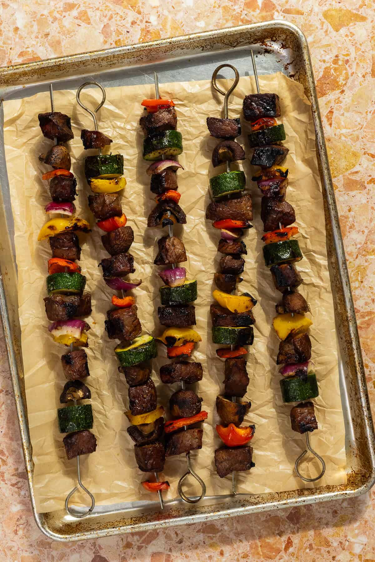 A parchment lined baking sheet with cooked beef kabobs.