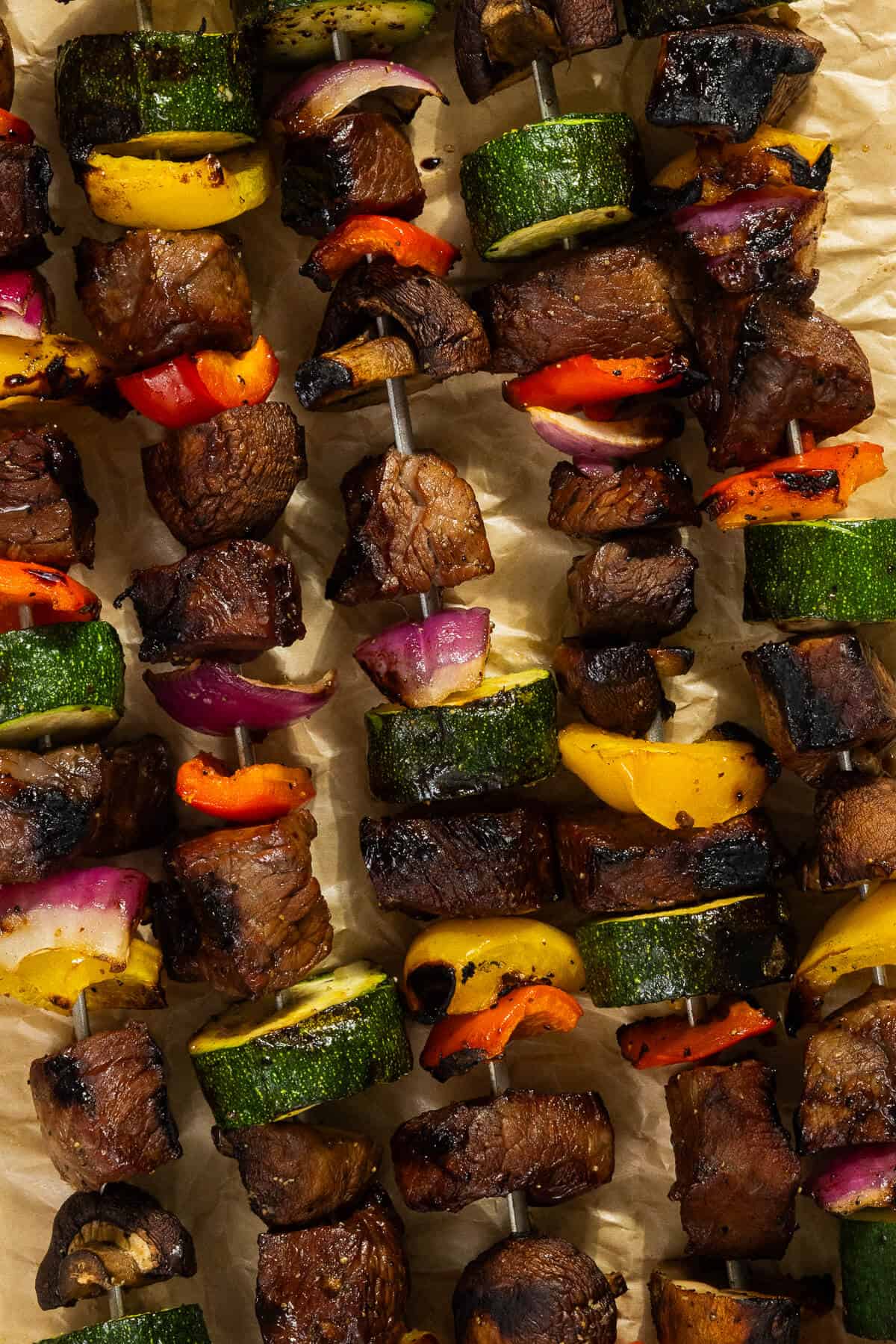 Five grilled beef kabobs on a baking sheet.