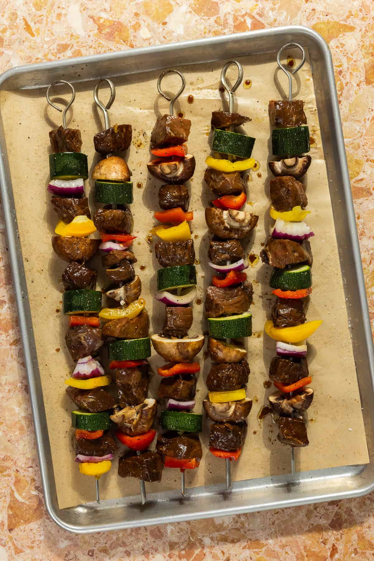 A parchment-lined baking sheet with beef kabobs.