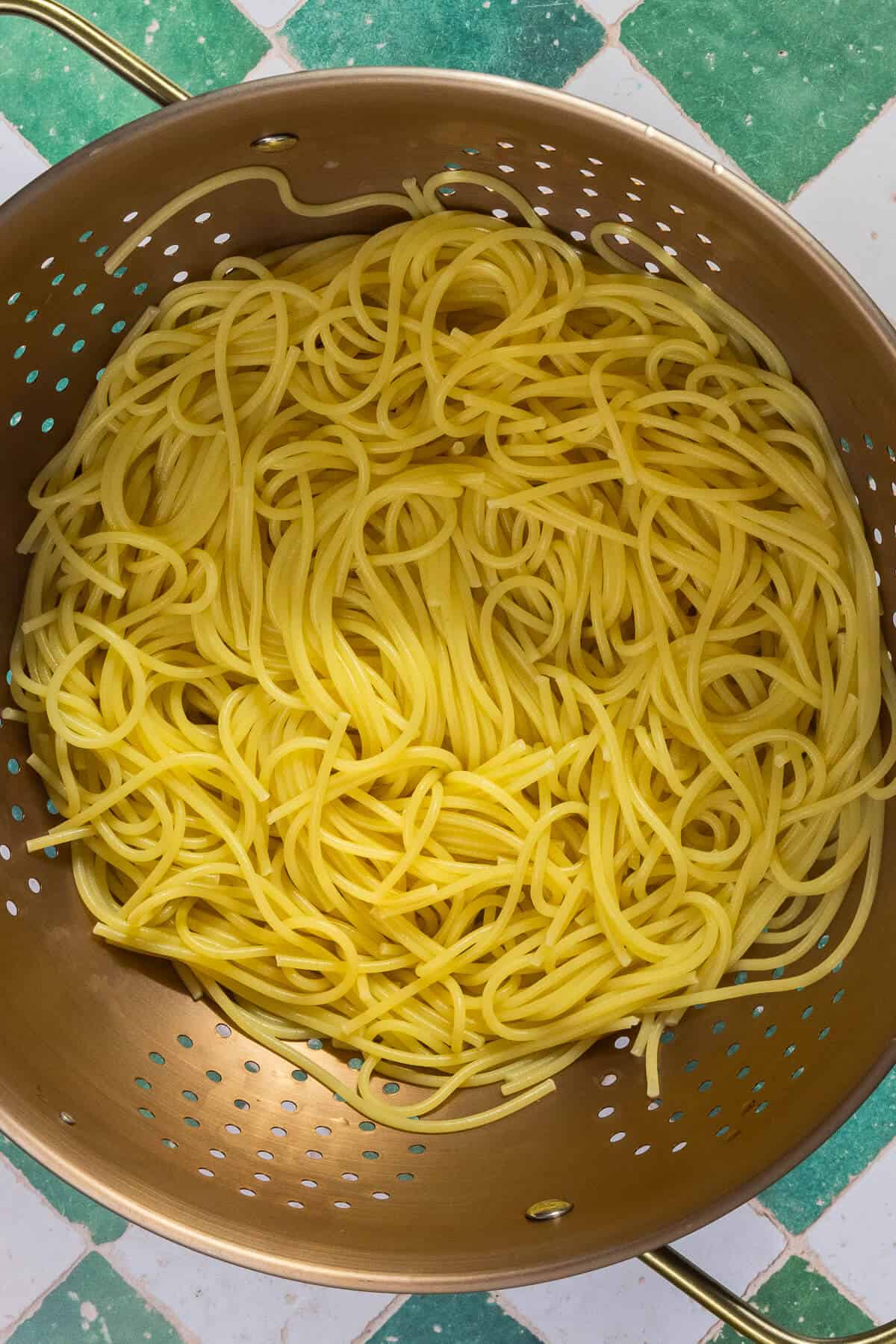 A large colander with cooked thin spaghetti noodles.