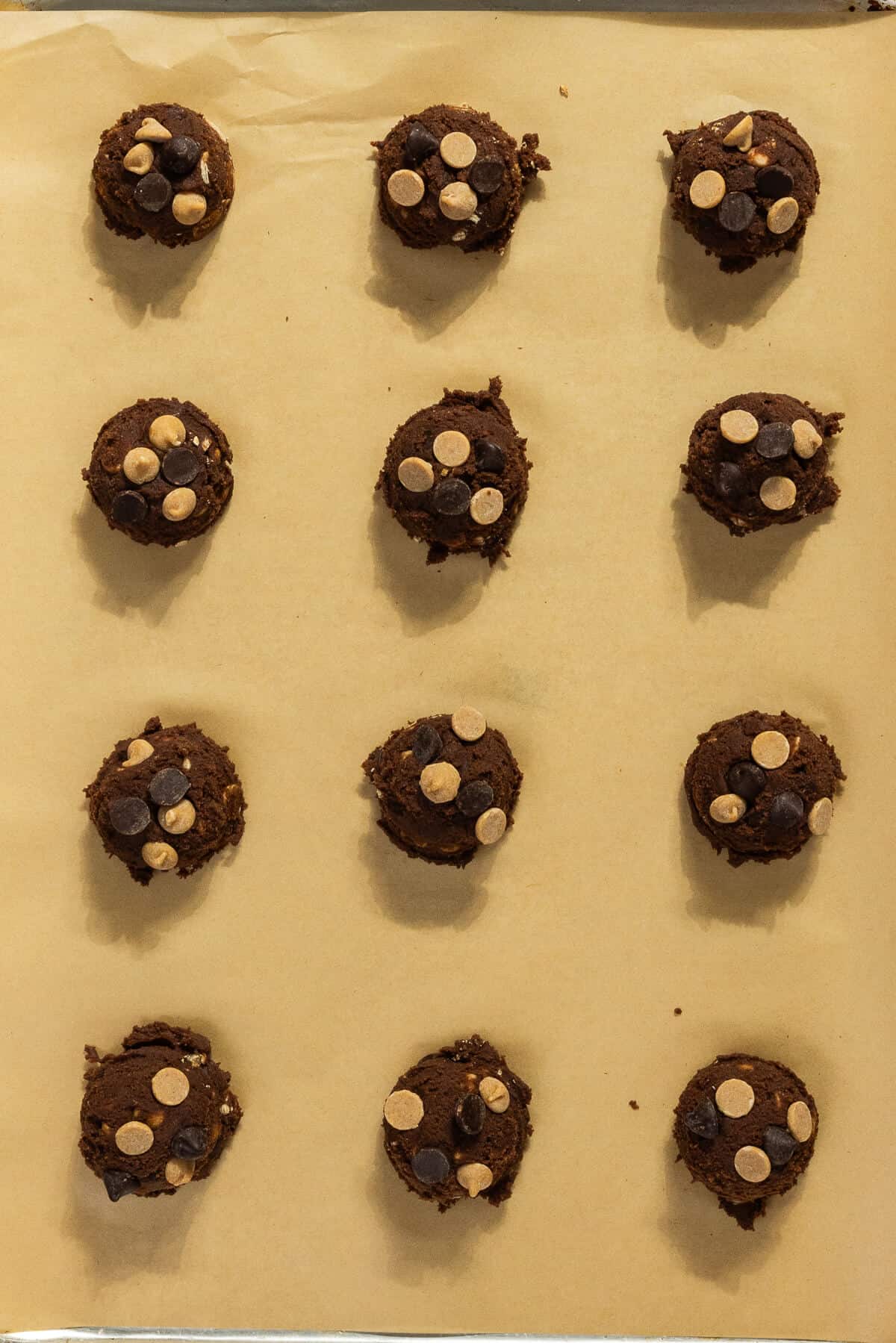 Twelve cookie dough balls on a parchment-lined baking sheet.