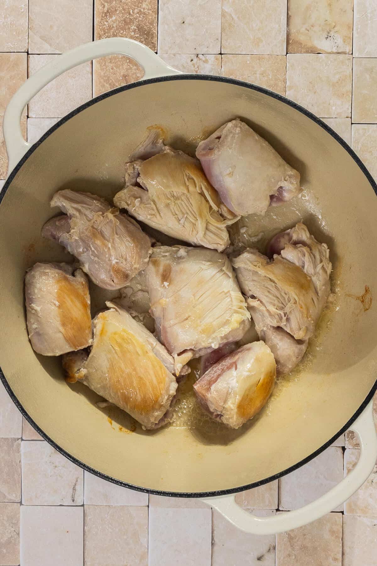 A large dutch oven pot with seared chicken thighs.