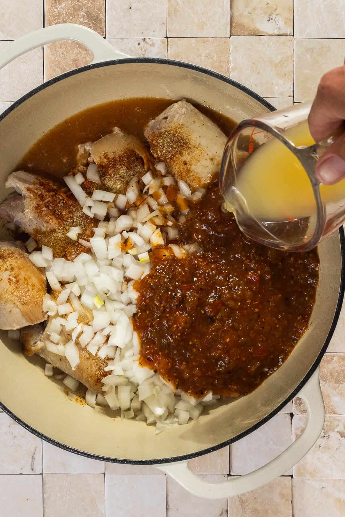 Chicken broth being poured into the dutch oven with the other ingredients.